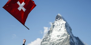 eine Schweizer Fahne wird in die Luft geworfen, im Hintergrund ein verschneiter Berg