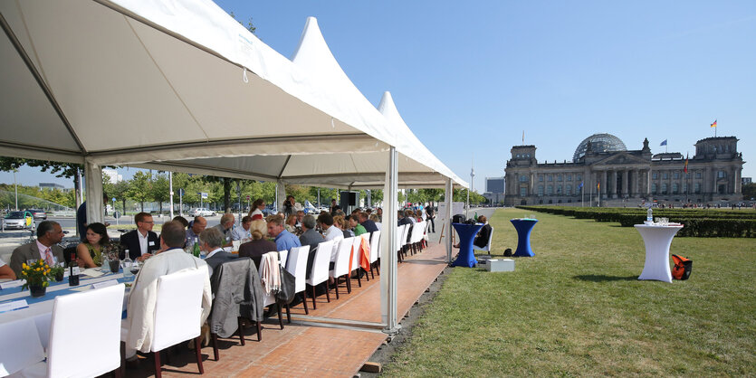 Vor dem Reichstag steht eine lange Tafel, daran sitzen Menschen