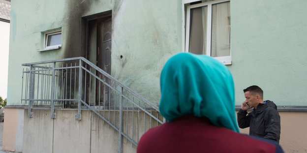 eine Frau mit Kopftuch vor der russgeschwärzten Moschee
