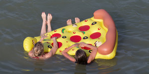Zwei Frauen hängen an einem aufblasbaren Stück Pizza und schwimmen auf dem Wasser