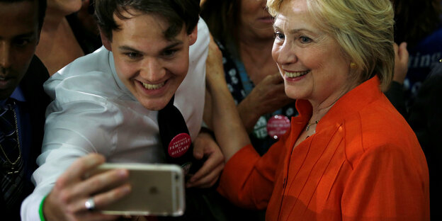 Ein männlicher, junger Fan macht ein Selfie mit Hillary Clinton