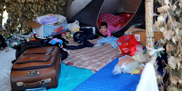 Vor einem Zelt liegen Decken und ein Koffer, in dem Zelt ein Baby