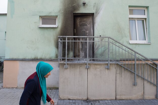 Eine Frau mit Kopftuch geht an einem Gebäude vorbei, dass Rauchspuren an dem Wänden aufweist