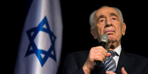 Peres mit Mikrofon im Porträt, daneben eine israelische Flagge
