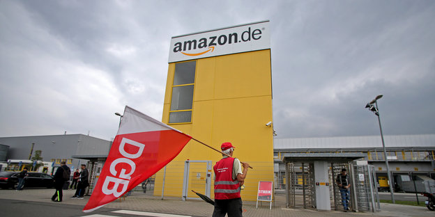 Mann mit DGB-Fahne vor einen Amazon-Firmentor