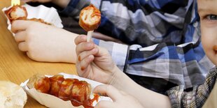 Ein Kind hält ein Stück Currywurst in die Höhe