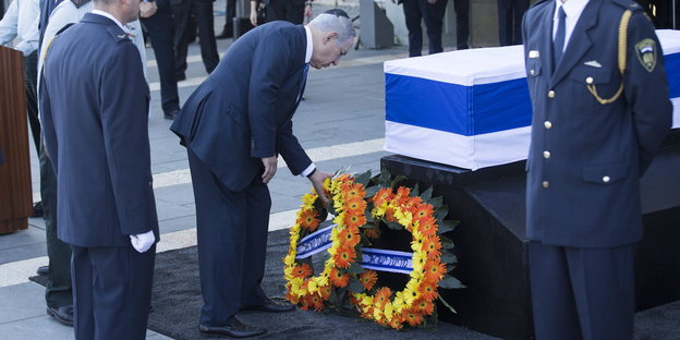 Benjamin Netanjahu bückt sich vor dem in eine Israel-Flagge eingehüllten Sarg von Schimon Peres und legt einen Kranz nieder