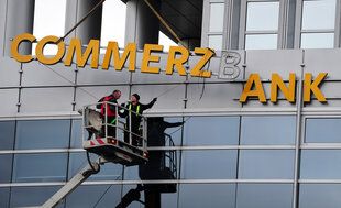 Zwei Männer auf einer Hebebühne zeigen auf den Schriftzug "Commerzbank", der abmontiert wird