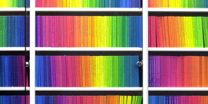 Mehrere Bücherregal überreinander, die voller Bücher sind, welche in Regenbogenfarben angeordnet stehen