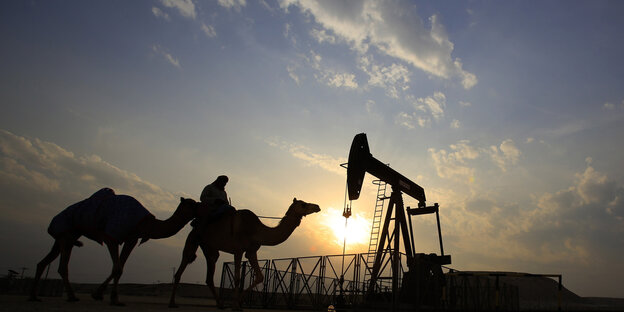 Eine Ölförderanlage und zwei Kamele im Sonnenuntergang