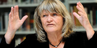 Frauenrechtlerin Alice Schwarzer steht mit erhobenen Händen vor einem Bücherregal