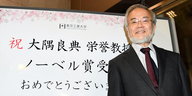 ein grinsender Mann vor einer Tafel mit japanischen Schriftzeichen