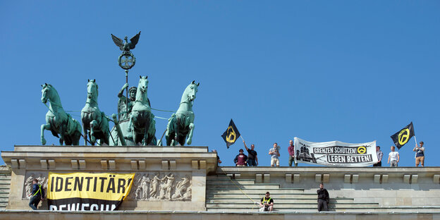Männer protestieren mit Fahnen, auf denen "identitäre Bewegung", auf dem Brandenburger Tor
