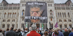 In einer Menschenmenge trägt eine Person ein Plakat auf dem Viktor Orban das Gesicht in den Händen begräbt
