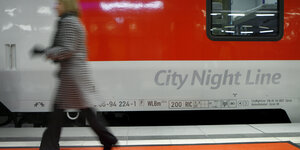 Eine Frau geht an einem Nachtzug der Deutschen Bahn entlang, der am Gleis steht.