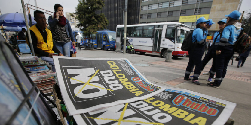 Zeitungstitel zeigen ein „No“, dahinter stehen Grüppchen von Menschen