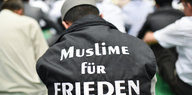 Ein Mann trägt den Kopf gesenkt und den Schriftzug Muslime für Frieden auf dem Rücken