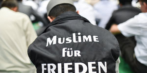 Ein Mann trägt den Kopf gesenkt und den Schriftzug Muslime für Frieden auf dem Rücken