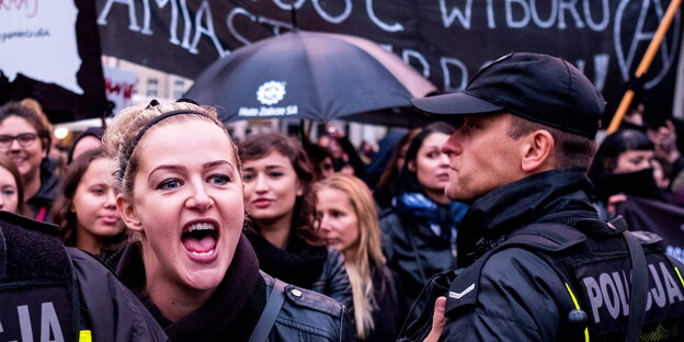 Eine Frau schreit, neben ihr steht ein Polizist, dahinter eine Menschenmenge