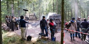 Eine Filmcrew steht im Wald vor Kohlenmeilern