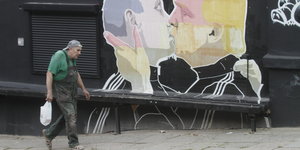 Ein Mann läuft vor einem Grafitti entlang, das Wladimir Putin und Donald Trump dabei zeigt wie sie sich innig küssen