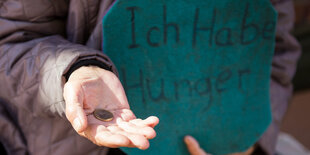 Eine ausgestreckte Hand, auf der eine Münze liegt, daneben ein Schild „Ich habe Hunger“