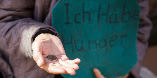 Eine ausgestreckte Hand, auf der eine Münze liegt, daneben ein Schild „Ich habe Hunger“