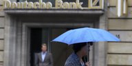 Eine Frau mit Regenschirm läuft an einer Filiale der Deutschen Bank vorbei.