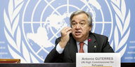 Porträt António Guterres. Er gestikuliert. Im Hintergrund: Das Symbol der UN