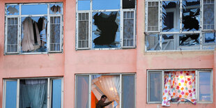 Sechs Fenster mit zetrümmertem Glas, aus einem weht eine bunte Gardine