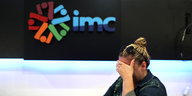 Eine blonde Frau weint und hält sich die Hand vor die Augen während sie vor einem Logo des geschlossenen türkischen Fernsehsenders IMC steht
