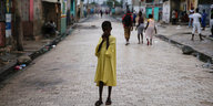 ein Kind in einem gelben Kleid steht allein auf der leergefegten Strasse