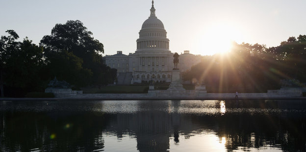 Hinter dem Capitol in Washington geht die Sonne auf, das Gebäude spiegelt sich im Wasser