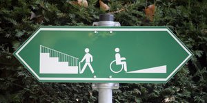 Ein Schild weist nach links zu einer Treppe und nach rechts zu einer Rollstuhlrampe.
