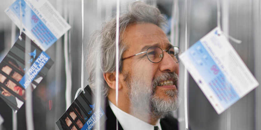 Can Dündar hinter an Schnüren aufgehängten Flyern