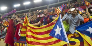 Fußballfans stehen auf der Besuchertribüne und halten die katalonische Flagge hoch