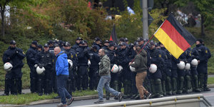 Zwei Männer laufen vor einer Hundertschaft. Einer hält die deutsche Nationalflagge in die Luft