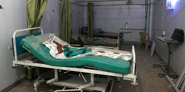 ein zerstörtes Krankenhauszimmer, auf dem vorderen Bett sind Blutspuren zu sehen