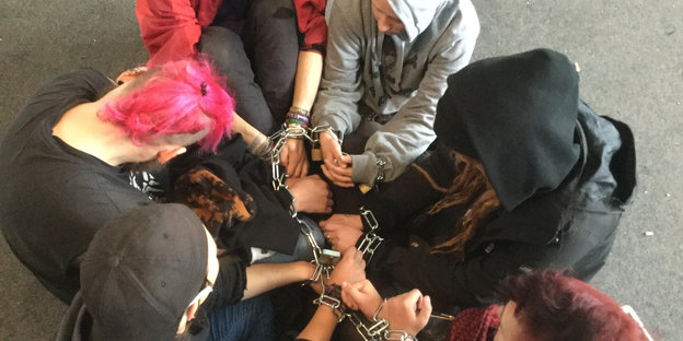 Fünf Jugendliche haben ihre Hände mit einer Kette zusammengeschlossen und sitzen auf dem Boden der geräumten "Kids" -Räume.