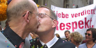 Zwei Männer küssen sich, dahinter ein Transparent „Liebe verdient Respekt“