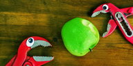 Zwei Beißzangen mit aufgeklebten Augen „essen“ einen grünen Apfel