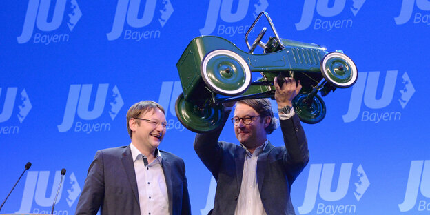 Andreas Scheuer hält ein grünes, großes Spielzeugauto in die Luft, Hans Reichhart steht daneben