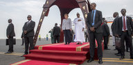 Angela Merkel steht neben Ibrahim Boubakar auf einem roten Teppich unter einem Baldachin