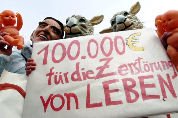 Demonstranten mit Schafs- und Schrödermasken, sowie Babypuppen und Plakat in der Hand