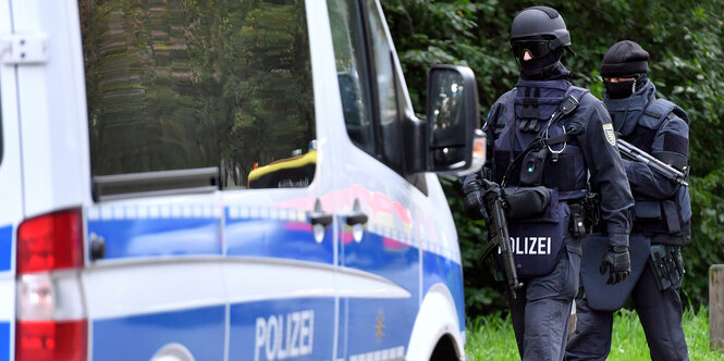 Zwei Polizisten in Schutzkleidung, vor ihnen ein großes Polizeifahrzeug