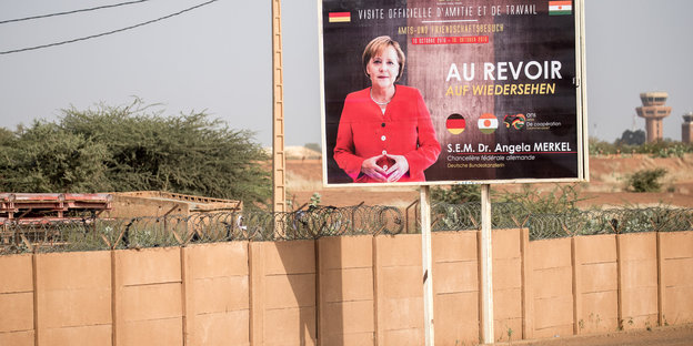 Ein Plakat steht vor einer Mauer. Darauf ist Angela Merkel zu sehen
