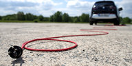 Ein rotes Kabel zum Laden eines E-Autos, das im Hintergrund zu sehen ist, liegt auf dem Boden