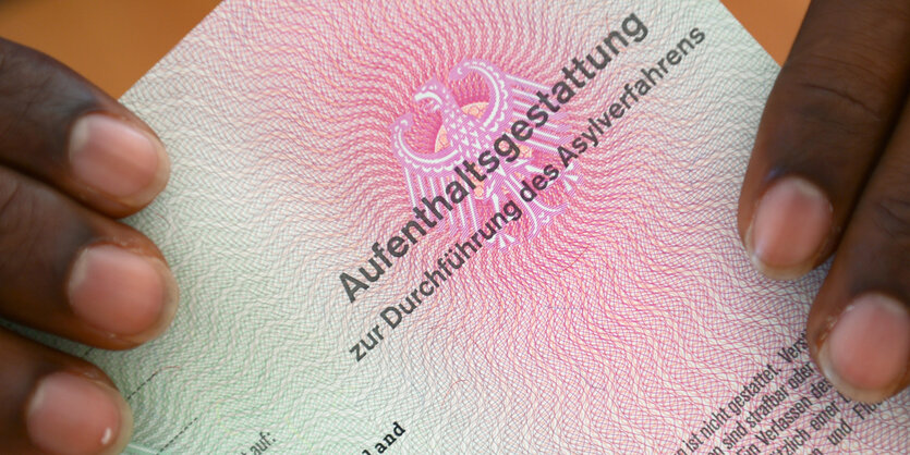 Eine Person hält ein Dokument mit der Aufschrift „Aufenthaltsgestattung“