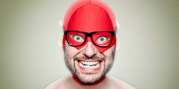 Ein Mann mit roter Superheldenmaske und irrem Grinsen.