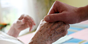 Eine Hand hält die einer bettlägerigen Seniorin